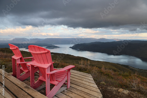 Two red adirondack chairs on a wooden deck overlooking Bonne Bay; Newfoundland and Labrador, Canada photo