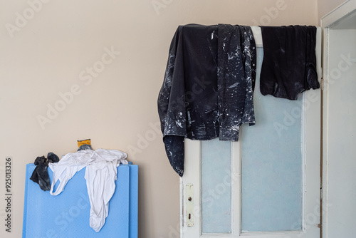 Workers' clothing soiled during renovation. Clothes covered in paint and cement stains hung over the door. Work gloves, undershirts, and socks thrown haphazardly on top of insulation foam.