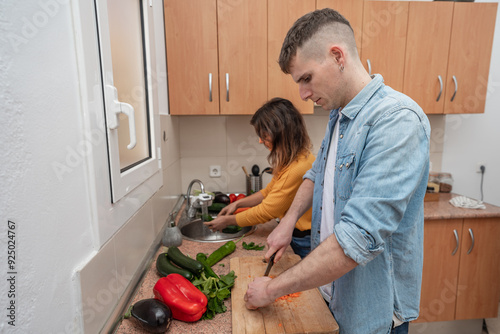 Young couple cooking together on a kitchen. Man and woman vegan cook vegetables for meal. Healthy lifestyle