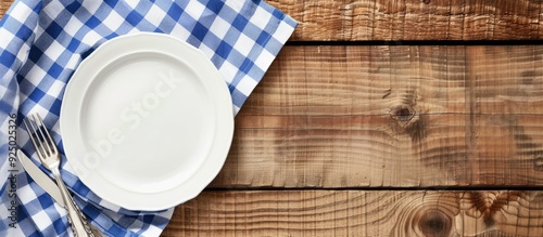 White plate on wooden table with blue checkered napkin. Flat lay, top view, with ample copy space image.