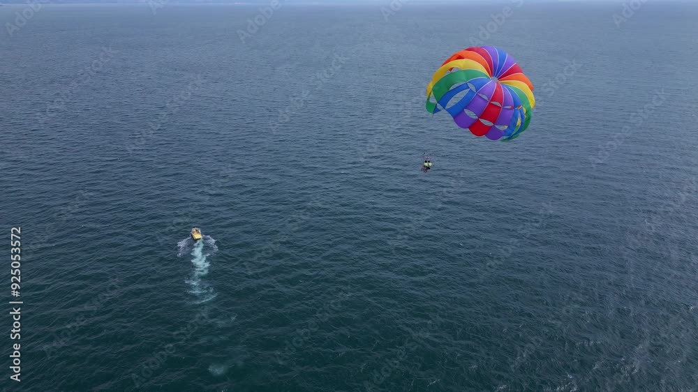 Drone video of a colorful parasail soaring over the open ocean, towed by a speedboat below. The aerial view captures the thrill and freedom of parasailing against a vast, serene seascape Drone video of a colorful parasail soaring over the open ocean, towed by a speedboat below. The aerial view captures the thrill and freedom of parasailing against a vast, serene seascape
