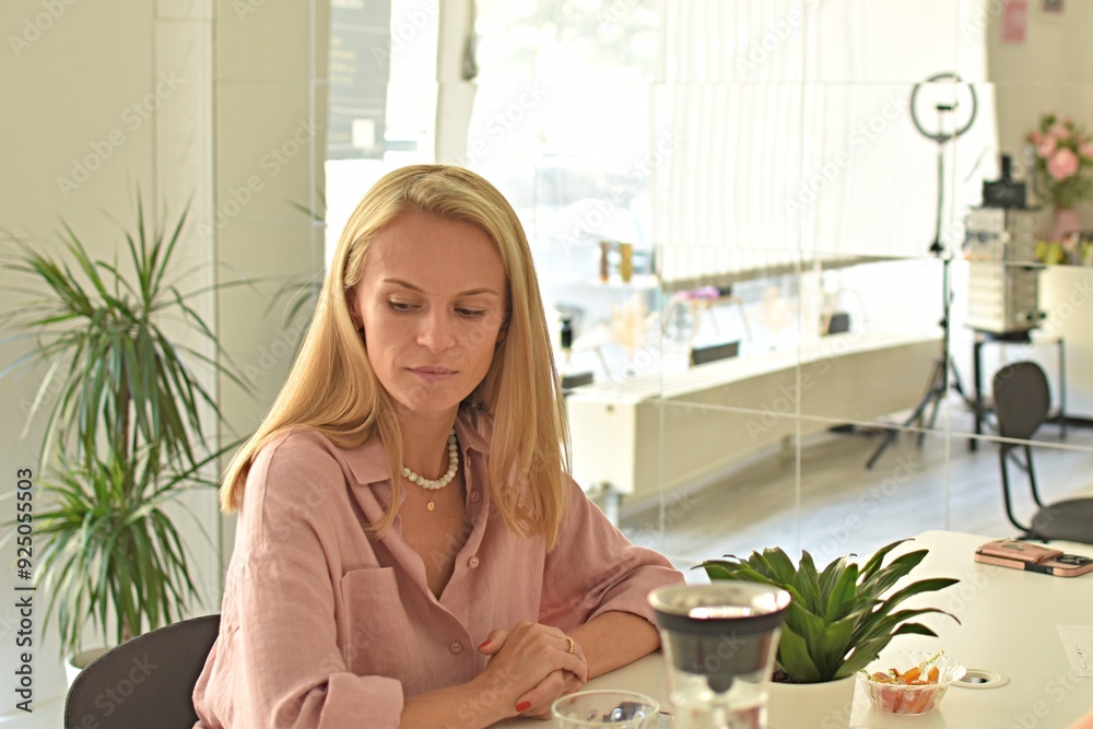 young woman with long blonde hair sitting at table and looking down young woman with long blonde hair sitting at table and looking down