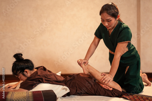 Asian woman professional masseuse service massaging a woman customer through traditional leg stretching techniques in spa and wellness center.