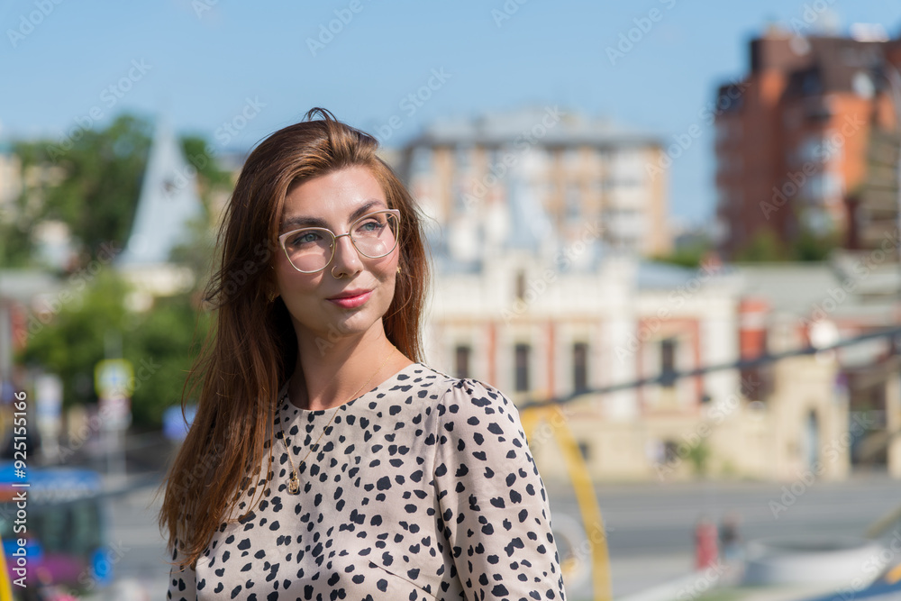 Close-up portrait of smiling beautiful long haired brunette woman in eyeglasses and leopard print dress standing on city street in a sunny summer day. Soft focus. People theme. Close-up portrait of smiling beautiful long haired brunette woman in eyeglasses and leopard print dress standing on city street in a sunny summer day. Soft focus. People theme.