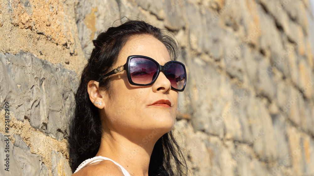 Stylish Woman in Sunglasses Relaxing Against a Rustic Stone Wall Stylish Woman in Sunglasses Relaxing Against a Rustic Stone Wall