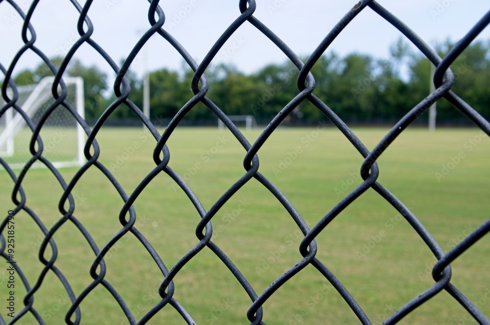 Looking through chain link fence at green field with soocer goals Looking through chain link fence at green field with soocer goals