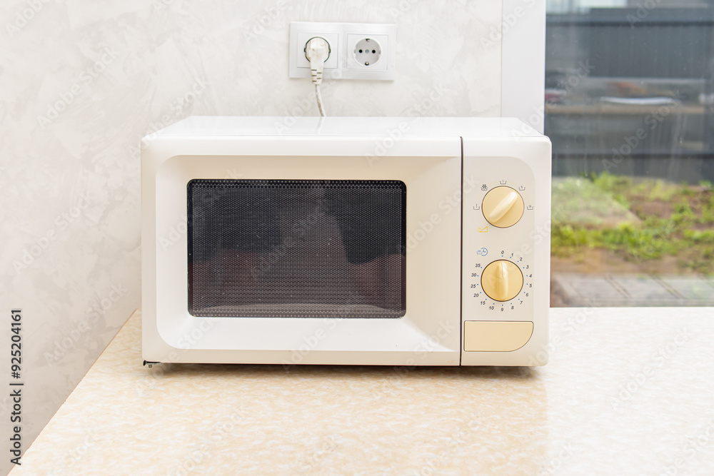 Microwave oven on table in the kitchen. White microwave oven with yellow power controls Microwave oven on table in the kitchen. White microwave oven with yellow power controls