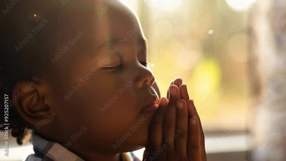 A child looks serene with eyes closed, hands together in prayer, illuminated by soft sunlight streaming through a window. A child looks serene with eyes closed, hands together in prayer, illuminated by soft sunlight streaming through a window.