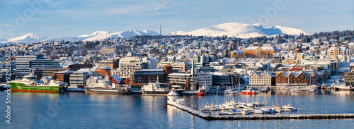 Panorama of norwegian city of Tromso in the winter. Snowy roofs, embankment near the port and fishing ships, Sunny winter day.