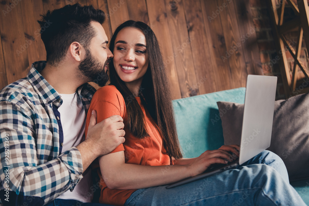 Photo of happy young couple move new place enjoy live together sit sofa netbook kiss cheeks new apartment room light house flat indoor Photo of happy young couple move new place enjoy live together sit sofa netbook kiss cheeks new apartment room light house flat indoor
