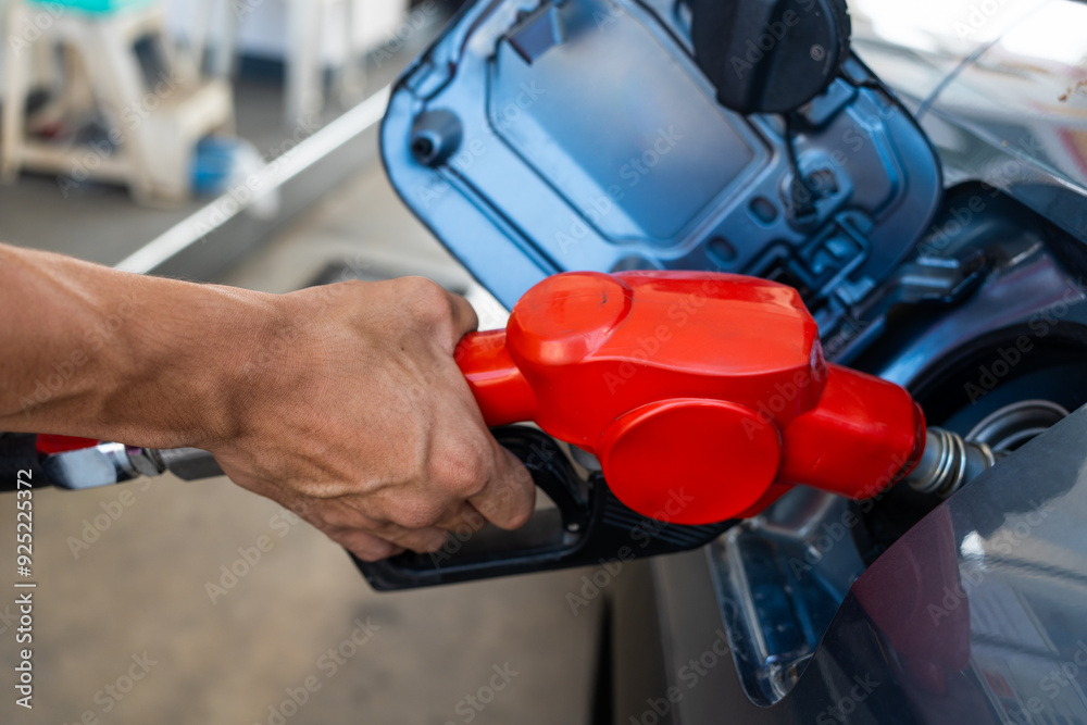 Fototapeta premium Refueling the car at a gas station fuel pump. Man driver hand refilling and pumping gasoline oil the car with fuel at the refuel station. Car refueling on petrol station. Fuel pump at the station