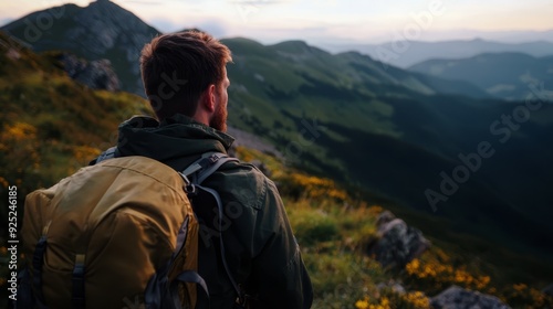  A man gazes at the mountain vistas fromoposition of a hilltop, his backpack at hand