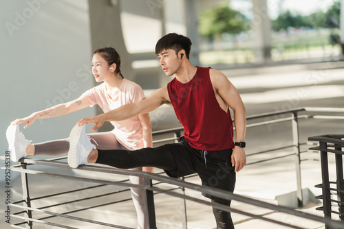 Active two Asian young athlete man and woman in sportswear doing stretching together before jogging exercise in urban area. Warming up for workout outdoor in the morning.