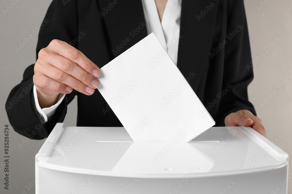 Woman putting her vote into ballot box against grey background, closeup Woman putting her vote into ballot box against grey background, closeup