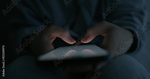 A woman uses a mobile phone while sitting in a dark room. Close-up of her hands, an unrecognizable person photo