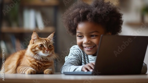 A smiling child engages with a laptop, while a playful cat observes nearby in a warm, inviting space filled with books photo