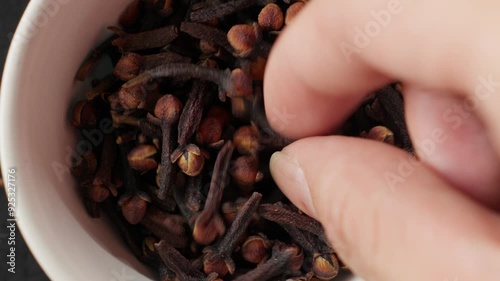 Hand picking dried cloves from a white bowl, capturing the aromatic spices up close photo