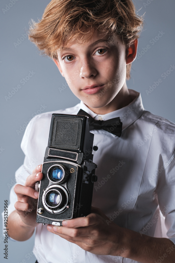 Fototapeta premium Preteen boy in white shirt and bow tie holding vintage photo camera
