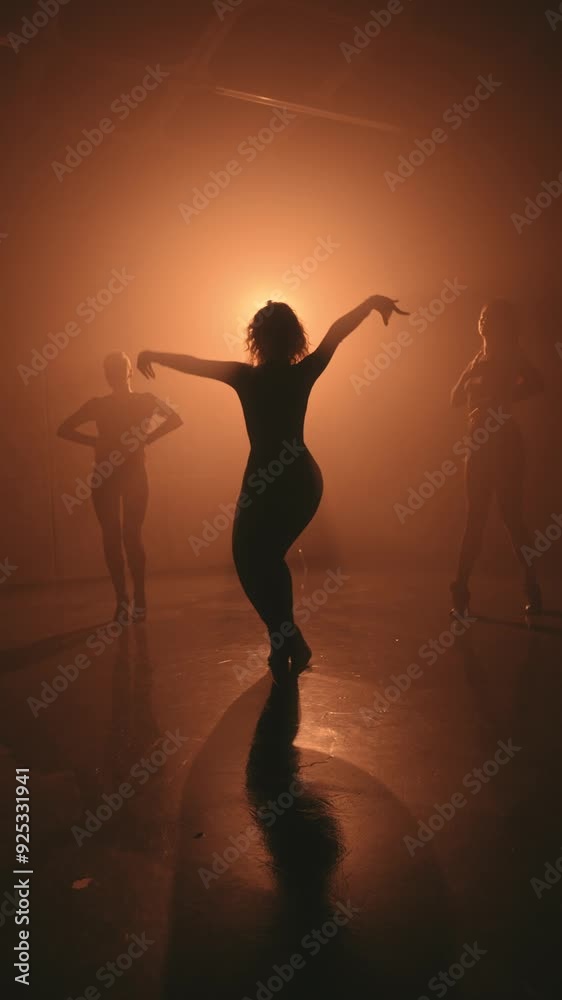 Silhouette of three women performing a dance in high heels, captured in a studio with a warm backlight.