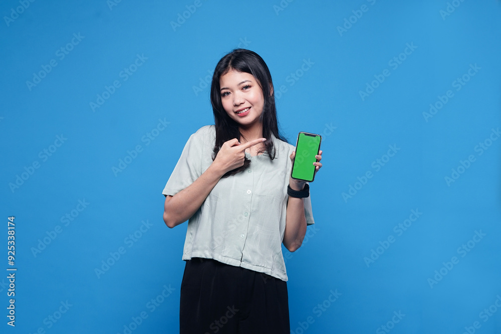Young Asia lady shows empty smartphone screen with positive expression, smiles broadly, dressed in casual clothing feeling happiness on blue background Young Asia lady shows empty smartphone screen with positive expression, smiles broadly, dressed in casual clothing feeling happiness on blue background