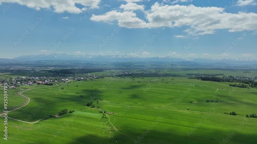Sunlit clouds above verdant lush meadow and Tatra Mountains scenic aerial