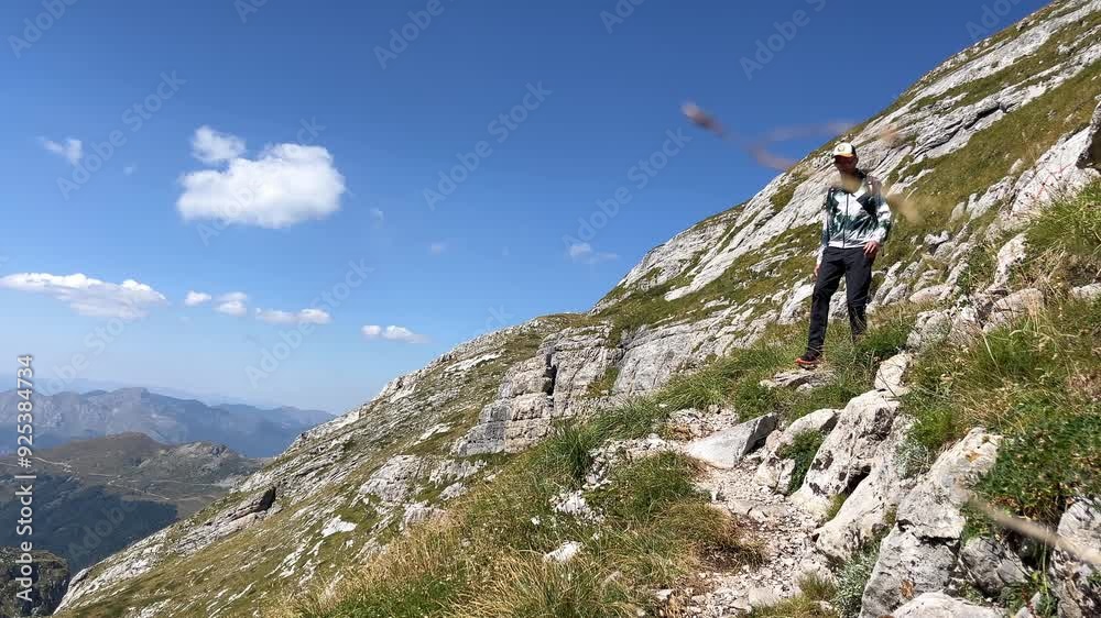 A tourist with a backpack and in light mountain clothes on a sunny day descends along a picturesque mountain path against the background of a blue sky A tourist with a backpack and in light mountain clothes on a sunny day descends along a picturesque mountain path against the background of a blue sky