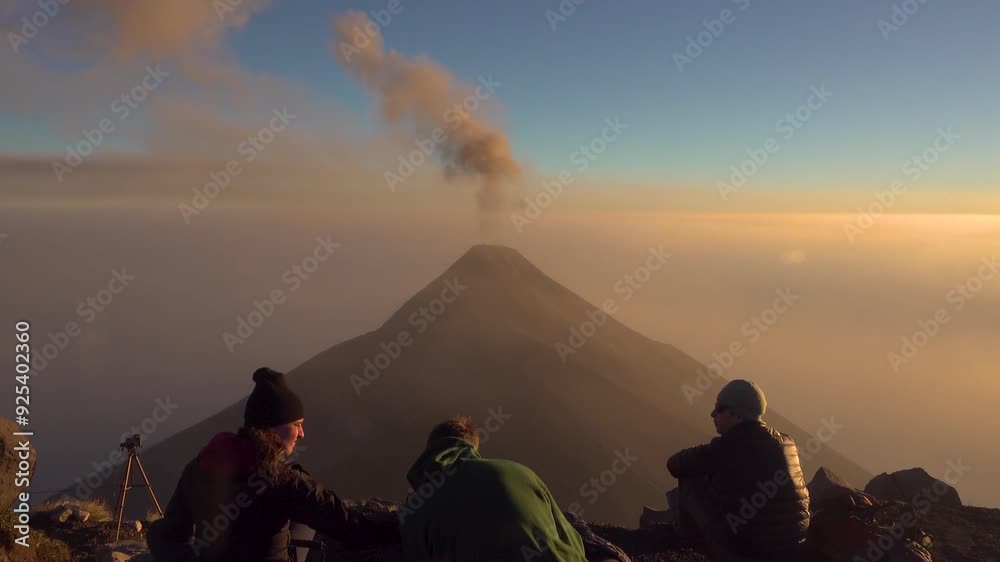 3 people watch smoke slowly come out of Fuego Volcano. Watching from Acatenango Volcano above the clouds at sunset