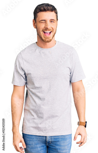 Handsome young man with bear wearing casual tshirt winking looking at the camera with sexy expression, cheerful and happy face.