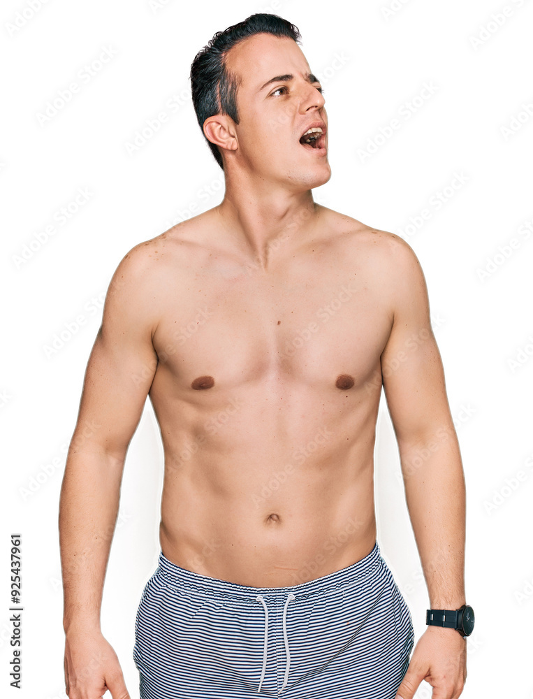 Fototapeta premium Handsome young man wearing swimwear shirtless angry and mad screaming frustrated and furious, shouting with anger. rage and aggressive concept.