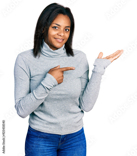 Beautiful hispanic woman wearing turtleneck sweater amazed and smiling to the camera while presenting with hand and pointing with finger.