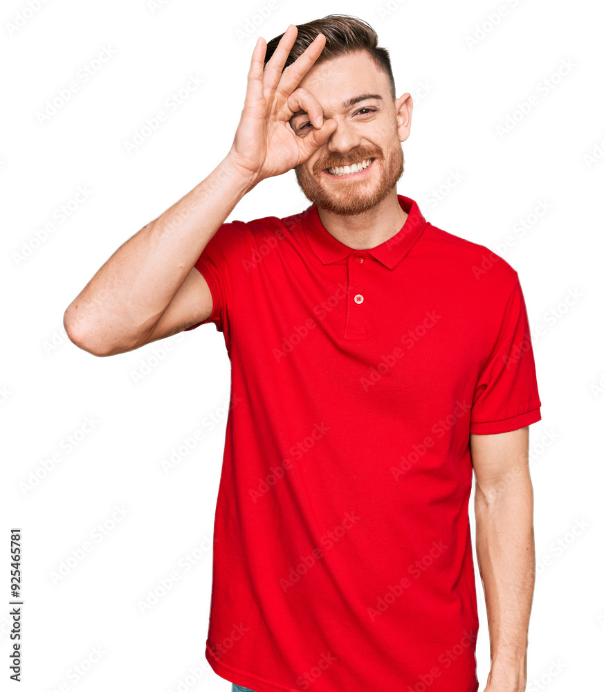 Young redhead man wearing casual clothes doing ok gesture with hand smiling, eye looking through fingers with happy face.