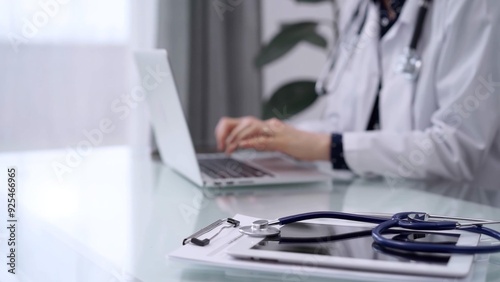 Tablet computer and blue stethoscope are on the glass table while doctor woman is using laptop computer on the glass table. Medicine concept