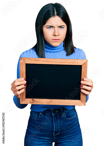 Young brunette woman with blue eyes holding blackboard skeptic and nervous, frowning upset because of problem. negative person.