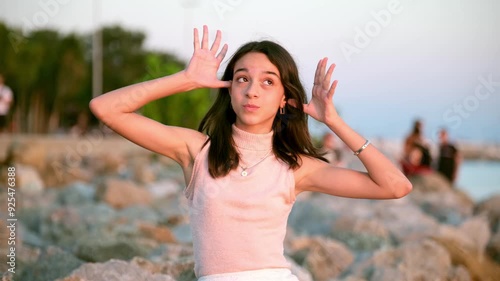 A dark-skinned teenage girl sitting on the rocks by the sea on a sunny summer day having fun making funny faces