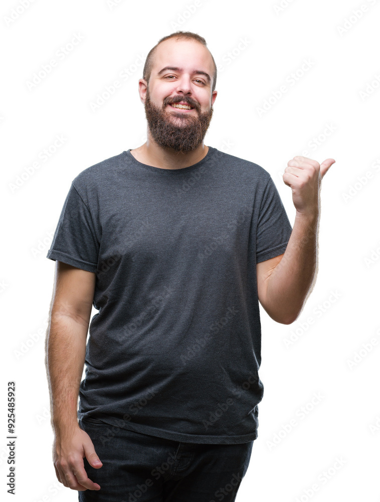 Young caucasian hipster man over isolated background smiling with happy face looking and pointing to the side with thumb up. Young caucasian hipster man over isolated background smiling with happy face looking and pointing to the side with thumb up.