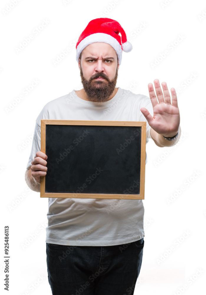 Young caucasian hipster man wearing christmas hat holding blackboard over isolated background with open hand doing stop sign with serious and confident expression, defense gesture Young caucasian hipster man wearing christmas hat holding blackboard over isolated background with open hand doing stop sign with serious and confident expression, defense gesture