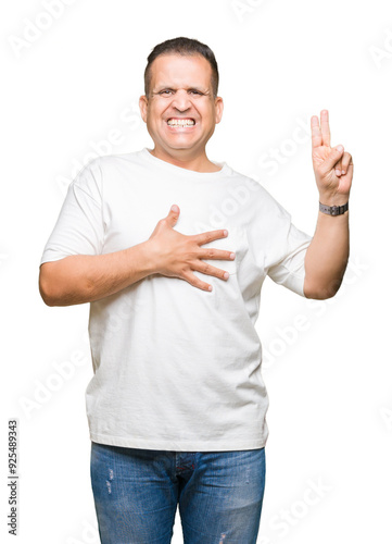 Middle age arab man wearig white t-shirt over isolated background Swearing with hand on chest and fingers, making a loyalty promise oath photo