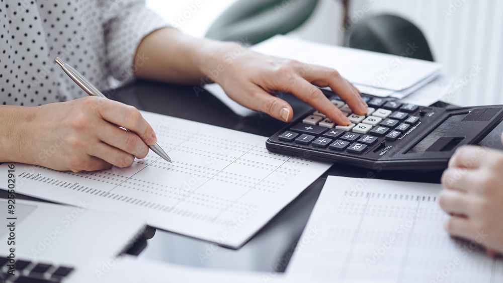 Fototapeta premium Woman accountant using a calculator and laptop computer while counting taxes with a client or a colleague. Business audit team, finance advisor