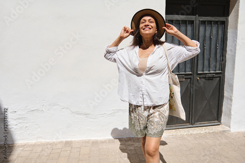 Joyful woman smiling in a sunny urban setting, enjoying a carefree day with her hat and tote bag outside a classic building photo