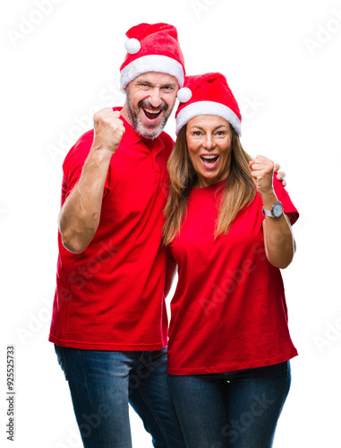 Middle age hispanic couple wearing christmas hat over isolated background celebrating surprised and amazed for success with arms raised and open eyes. Winner concept. photo