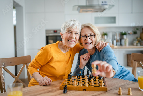 two women mature senior females sisters play chess board game at home