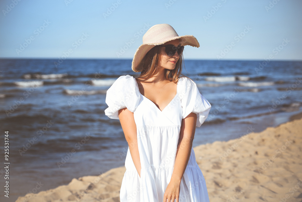 Happy smiling blonde woman is posing on the ocean beach with sunglasses and a hat Happy smiling blonde woman is posing on the ocean beach with sunglasses and a hat