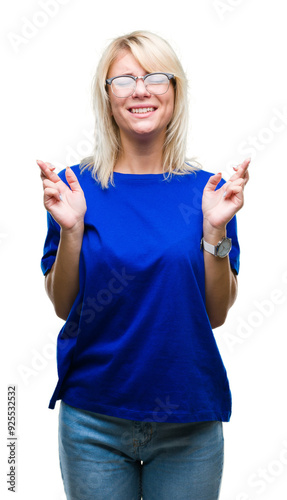 Young beautiful blonde woman wearing glasses over isolated background smiling crossing fingers with hope and eyes closed. Luck and superstitious concept.