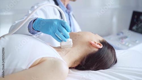 Doctor man wearing blue medical gloves is using ultrasound equipment on neck of female patient lying down for a medical examination