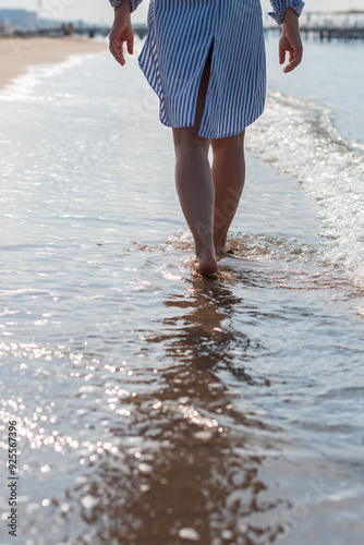 young woman barefoot walks along the sandy beach by the sea at sunset, plunging her feet into the waves and sand, pleasant relaxation on summer vacation