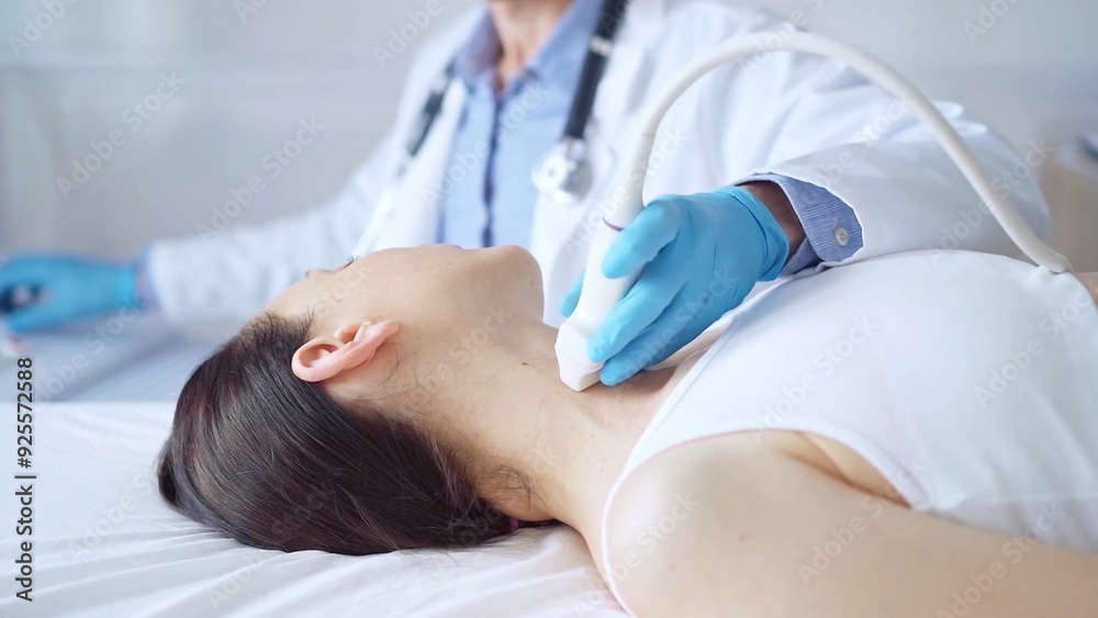 Doctor man wearing blue medical gloves is using ultrasound equipment on neck of female patient lying down for a medical examination Doctor man wearing blue medical gloves is using ultrasound equipment on neck of female patient lying down for a medical examination