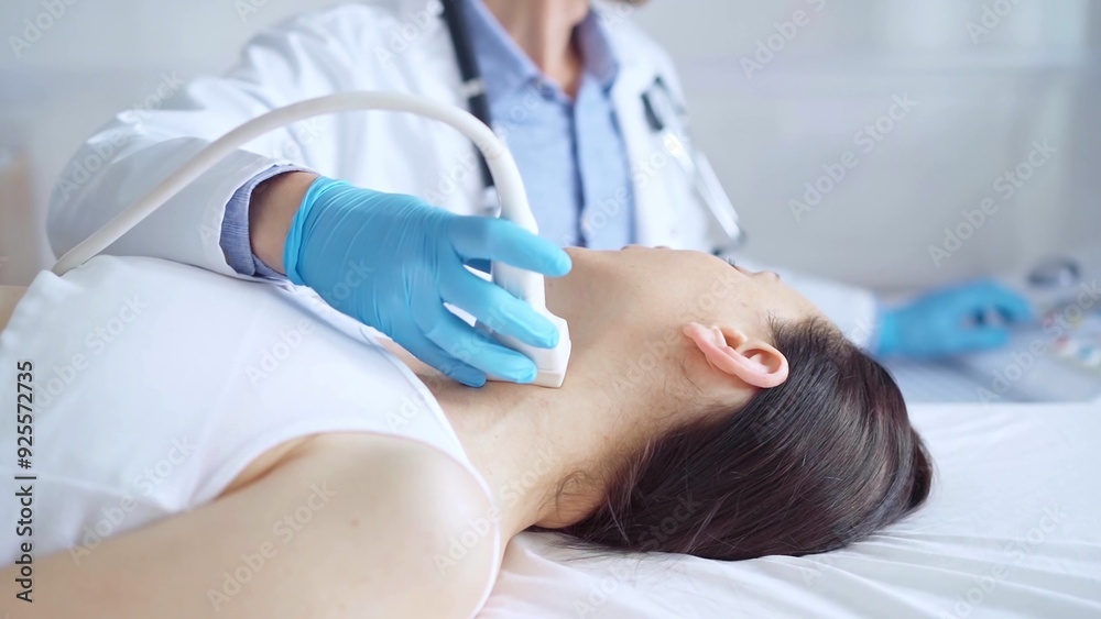 Obraz premium Doctor man wearing blue medical gloves is using ultrasound equipment on neck of female patient lying down for a medical examination