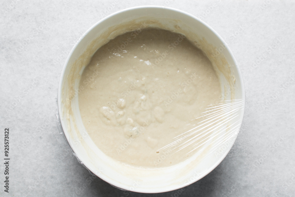 Overhead view of nigerian puff-puff dough being mixed with a wooden spoon, puff-puff dough in a white mixing bowl, process of making puff-puff or bofrot Overhead view of nigerian puff-puff dough being mixed with a wooden spoon, puff-puff dough in a white mixing bowl, process of making puff-puff or bofrot