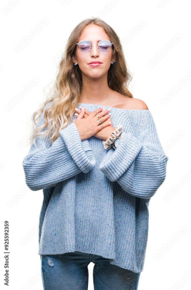 Beautiful young blonde woman wearing sunglasses over isolated background smiling with hands on chest with closed eyes and grateful gesture on face. Health concept. Beautiful young blonde woman wearing sunglasses over isolated background smiling with hands on chest with closed eyes and grateful gesture on face. Health concept.
