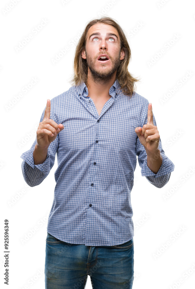 Obraz premium Young handsome man with long hair over isolated background amazed and surprised looking up and pointing with fingers and raised arms.